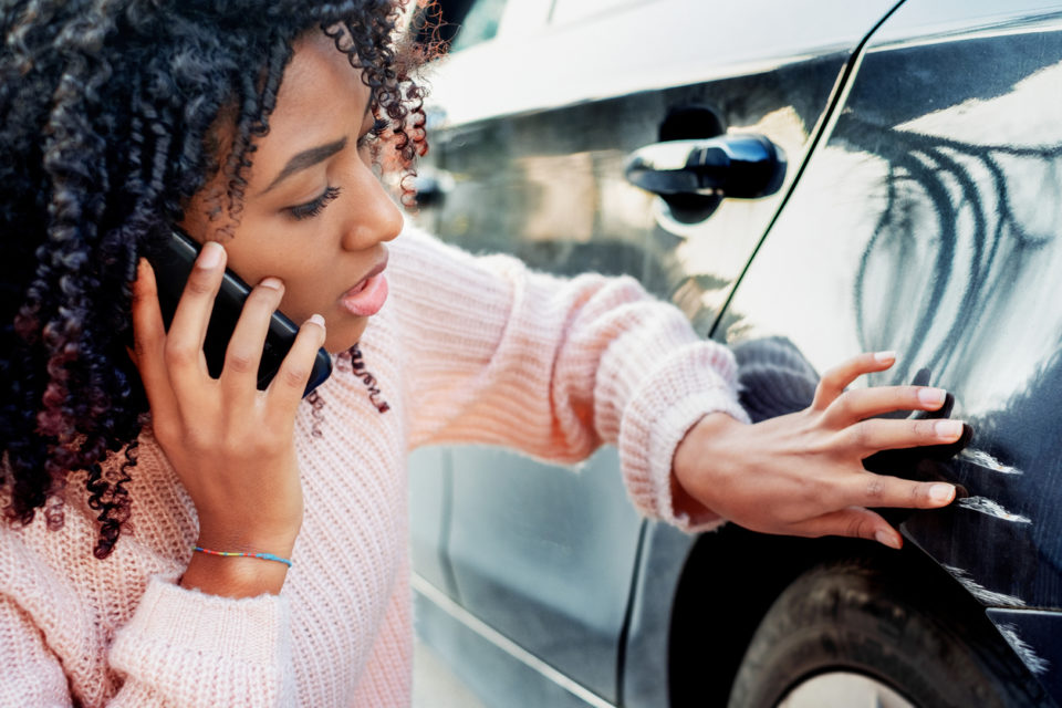 Woman on the phone inspecting damage to the side of her car