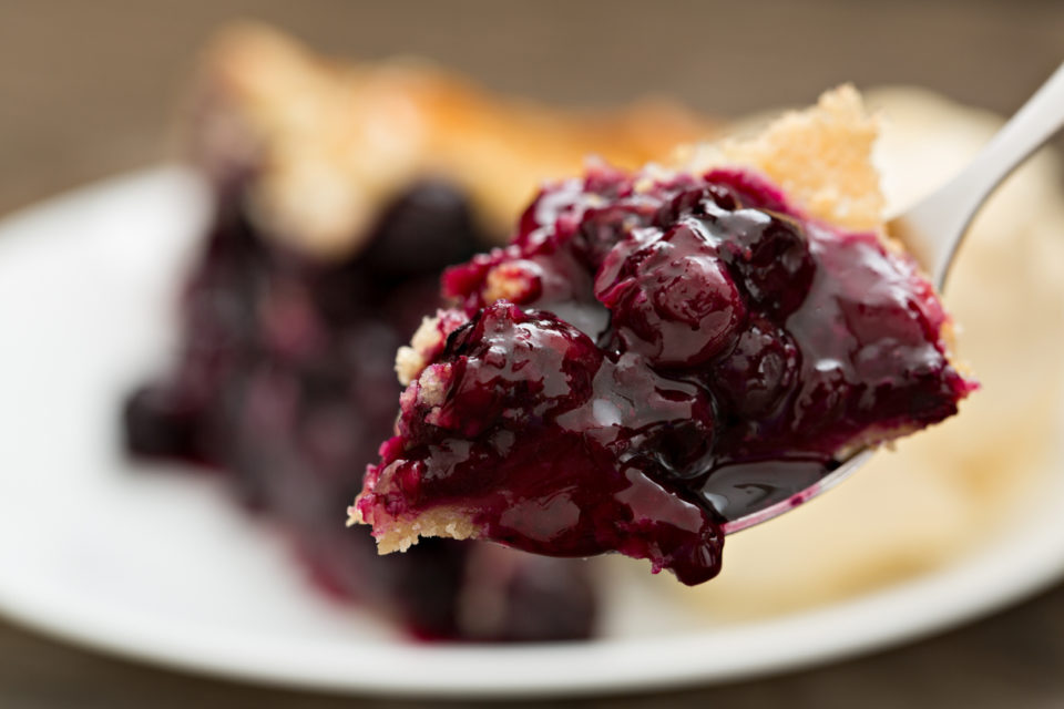 A high angle close up shot of a bite of blueberry pie on a fork.