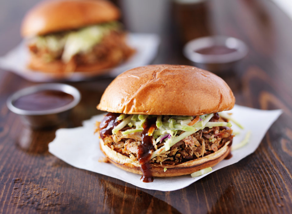 two pulled pork barbecue sandwiches shot with selective focus and on top of wooden table.