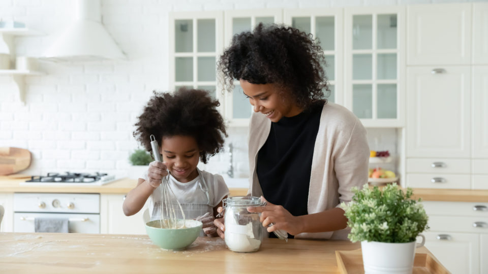 Happy mom and daughter bake in kitchen together