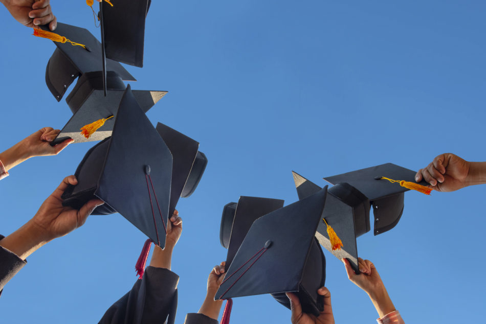 College grads holding up their caps 