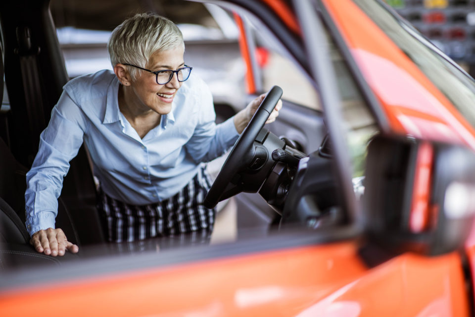 Happy mature woman buying a car in a showroom.