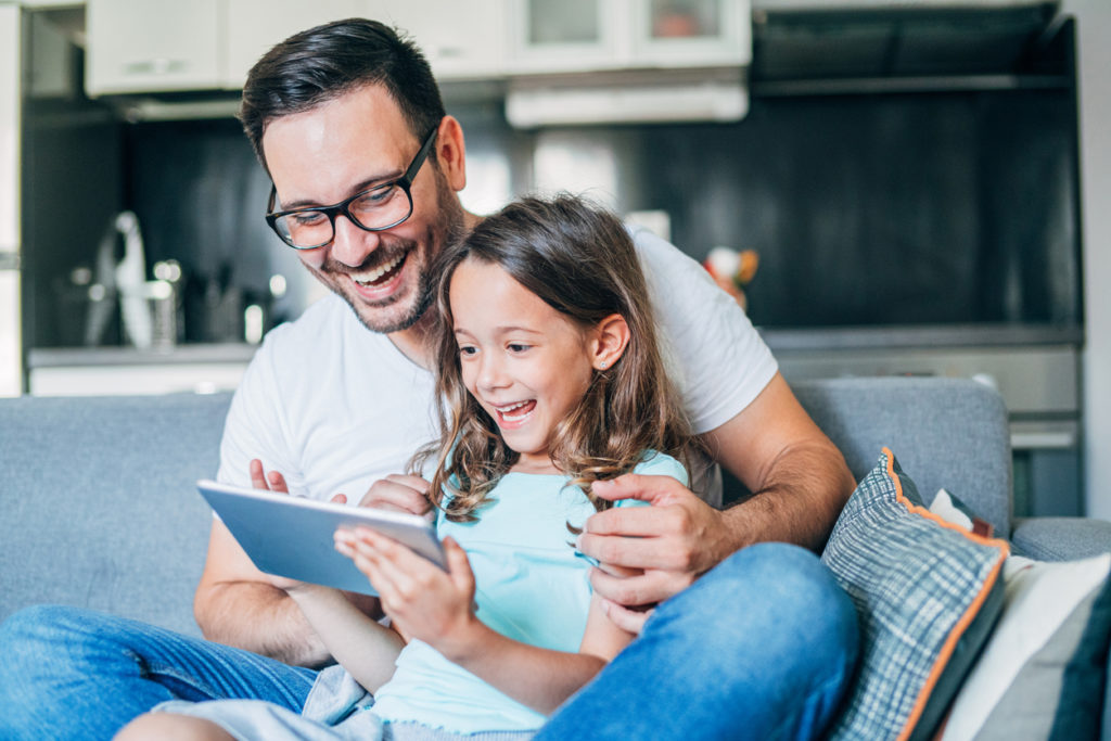 Father and his daughter having fun with digital tablet on couch.