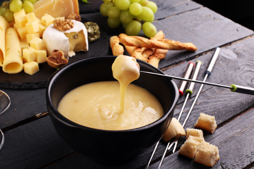 Gourmet Swiss fondue dinner with assorted cheeses on a board alongside a heated pot of cheese fondue