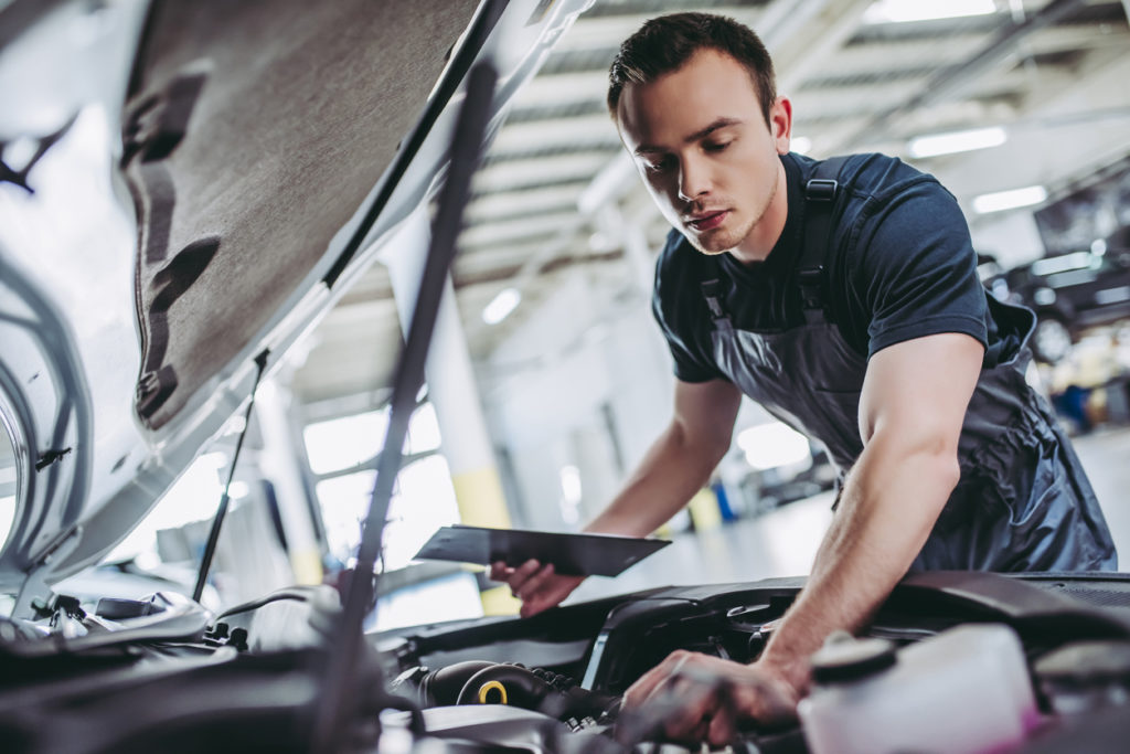 mechanic in uniform is examining the car while working in auto service.