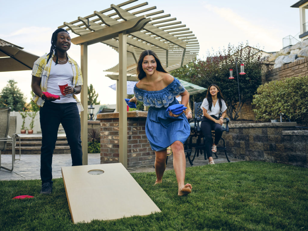 A group of friends playing a Cornhole bean bag toss game in a backyard of a home.